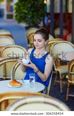 Beautiful young Parisian woman in blue blouse drinking coffee in an outdoor cafe on a summer day