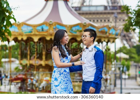 Young romantic Asian couple having a date near the traditional French merry-go-round, Eiffel tower is in the background, Paris, France