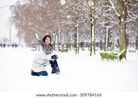 Beautiful young woman in Paris in the Tuileries garden, enjoying beautiful winter day and snow falling from the sky. Rare snowy day in Paris