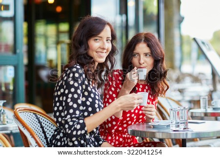 Beautiful twin sisters drinking coffee in a cozy outdoor cafe in Paris, France. Happy smiling girls enjoy their vacation in Europe