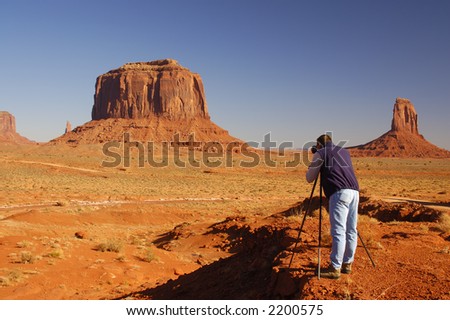 A photographer in blue jeans and dark blue vest is photographing buttes in Monument Valley park (Navajo Nation, Utah).