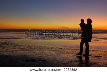 Daughter in her mother\'s arms silhouetted at sunset at Pacific. Mother\'s left leg is motion-blurred.