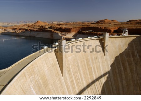Glen Canyon Dam in Page, Arizona lit by morning sun with cars parked on the road running along its\' top.