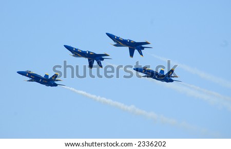 4 Blue Angels Flight Team planes in tight formation at air show - pilots in yellow helmets visible.