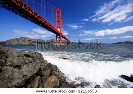 Surf splashes over rocks under Golden Gate Bridge as seen from the Fort Point beach.