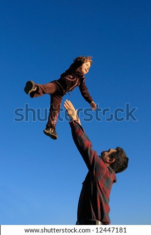 A happy two year old girl tossed into the blue sky by her father (portrait (vertical) orientation).