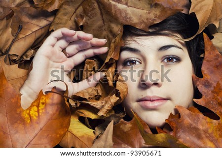 Close view of the face of a beautiful girl surrounded by autumn leaves.
