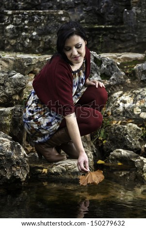 Young beautiful woman playing with autumn leaf on a pond.