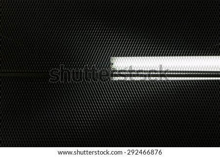 Close view of a fluorescent lamp in the ceiling through a metal grid.