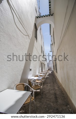 View of a narrow street of Tavira city with restaurant tables.