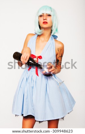 Attractive model woman in blue wig and red high heels pouring wine in a glass isolated on white