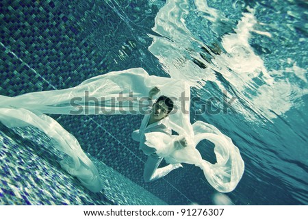 Man model swimming underwater with a long white cloth in an underwater photo session