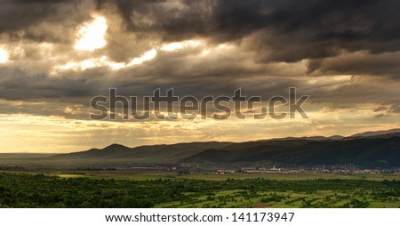 Storm scene with dark clouds and sunbeam on a field.