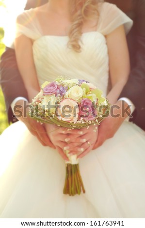 Beautiful wedding bouquet in hands of the bride and groom holding the bride\'s hands.
