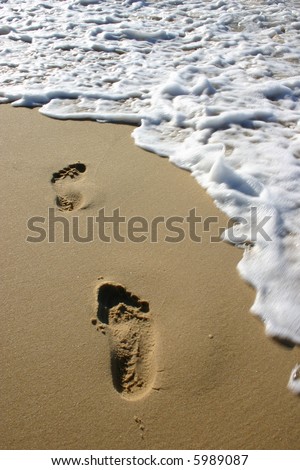 Foot prints at the beach about to be washed away by a wave,