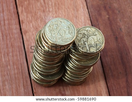 Two piles of Australian one dollar coins on a wooden background. Shallow depth of field focus.