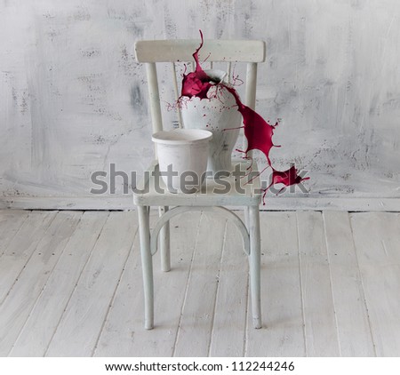 Splash of red paint from a pitcher standing on a white chair. Abstract composition of white objects in a white interior.