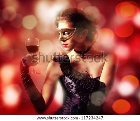 Masquerade. A beautiful young lady in a mask with a glass of red wine on the background bokeh.