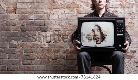 TV with a picture of the girl -facing through a hole in the hands of a seated man .