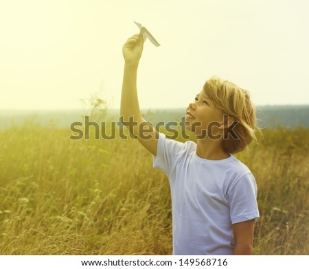 Happy kid playing with toy airplane against blue summer sky background.