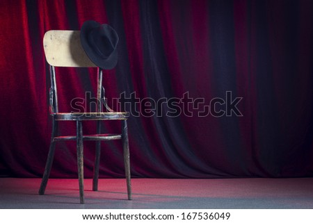 Retro chair with a black felt hat against a red curtain.