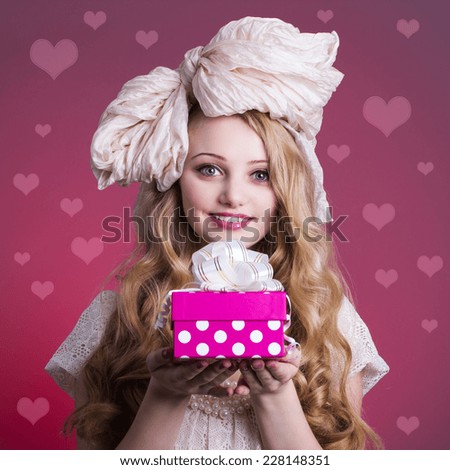 Portrait of a girl doll with gift box on pink background.