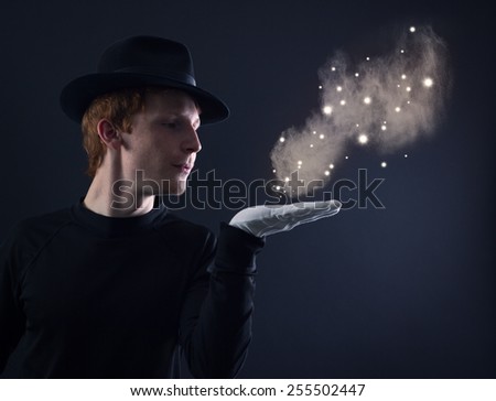 Portrait of a young magician in a black hat and white gloves on a dark background.