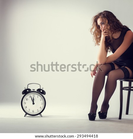 Frustrated young woman sitting on a chair looking at the clock.