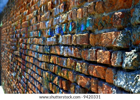 The time erodes an old red brick wall in the city. The bricks are eaten away, and the writings are indistinguishable