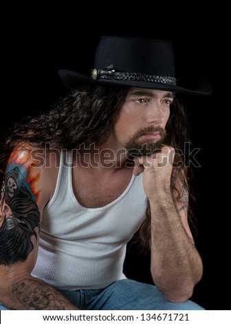 tough sexy man with long hair and tattoos wearing a black cowboy hat isolated on black