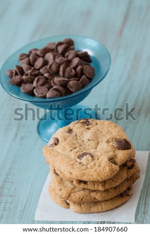 A stack of chocolate chip cookies with bowl full of chocolate chips