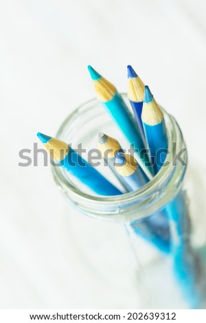 Pastel cool blue color pencils in glass jar on white from above