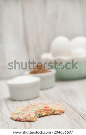 Colorful birthday confetti cookie with a bite taken out with eggs in a bowl and sugars