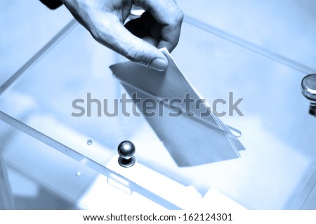 Hand putting a blank ballot inside the box, elections concept, BLUE TONE