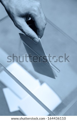 Hand putting a blank ballot inside the box, elections concept, blue tone