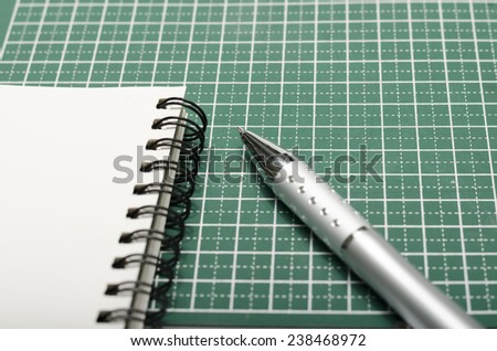 notebook and pen on green cutting mat