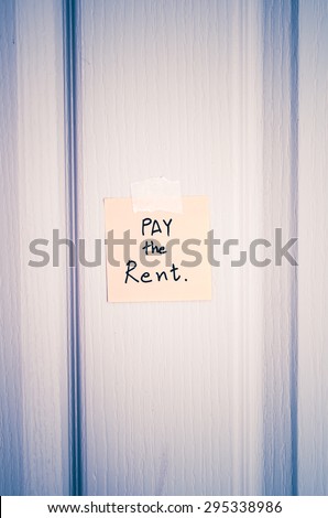 sticky note write a message pay the rent on wood door background vintage style