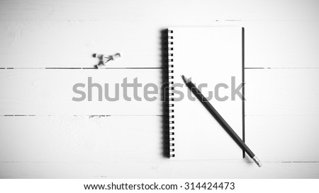 pencil and notepad with push pin over white table view from above black and white color style