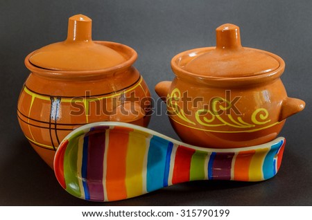 Two brown clay pots with colored ceramic spoon isolated on black background