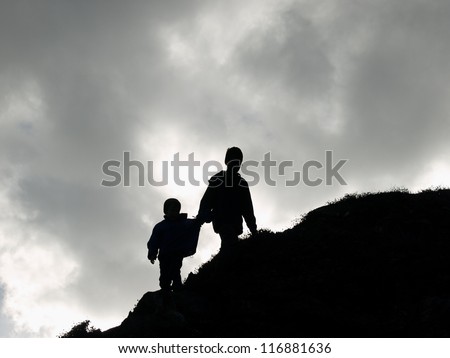 Two boys playing outside, climbing up a hill, silhouette, bad weather