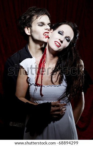 Male Vampire bites into the ear of a female, innocent human. He already has bitten her neck and lots of blood is flowing down.