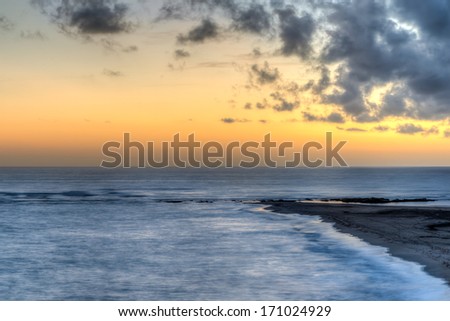 Beautiful orange ocean sunset lighting up the horizon above a deserted beach with calm surf in a tranquil marine background
