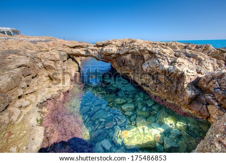 Natural rock arch over a tidal pool at the seaside with beautiful crystal clear water showing the underwater ecosystem with colourful seaweed and aquatic life