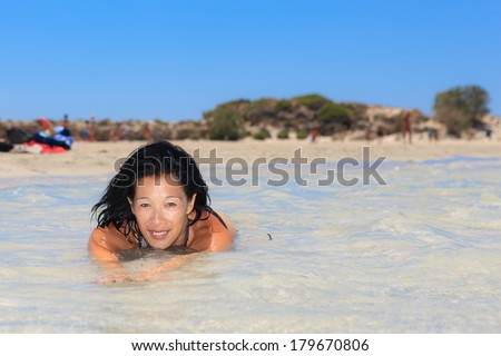 Attractive young woman enjoying a swim in the sea on a hot summer day off a golden sandy tropical beach smiling as she looks of to the side of the frame
