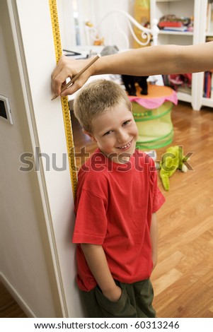 Smiling blond young boy getting height measurement in doorway