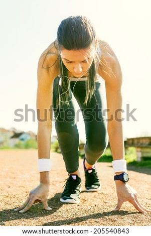 Young sports woman in start position preparing to run.