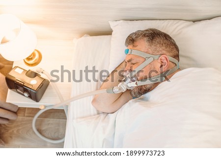 Sleeping man with chronic breathing issues considers using CPAP machine in bed. Healthcare, Obstructive sleep apnea therapy, CPAP, snoring concept Photo stock © 
