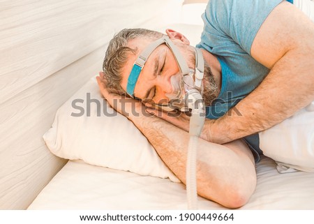 Sleeping man with chronic breathing issues considers using CPAP machine in bed. Healthcare, Obstructive sleep apnea therapy, CPAP, snoring concept Photo stock © 