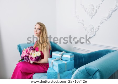 blonde girl with spring flowers and presents is sitting on blue sofa