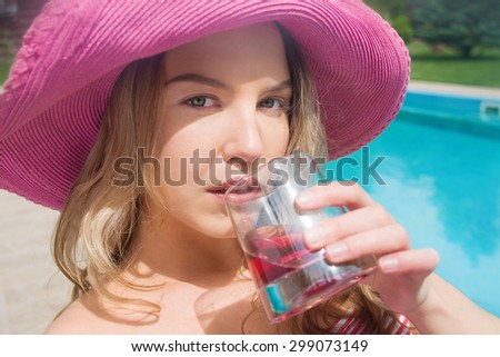 young blonde beautiful woman in pink hat spending her time drinking cocktail near swimming pool